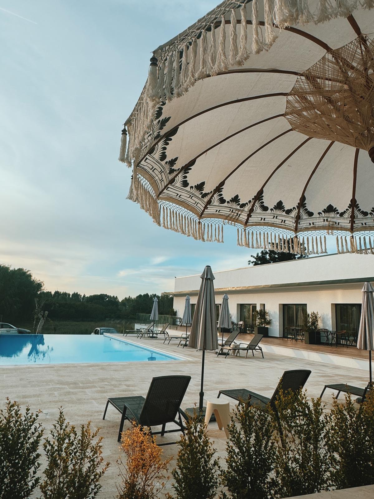 Piscina e terra&ccedil;o do alojamento ao entardecer, sob um guarda-sol de franjas