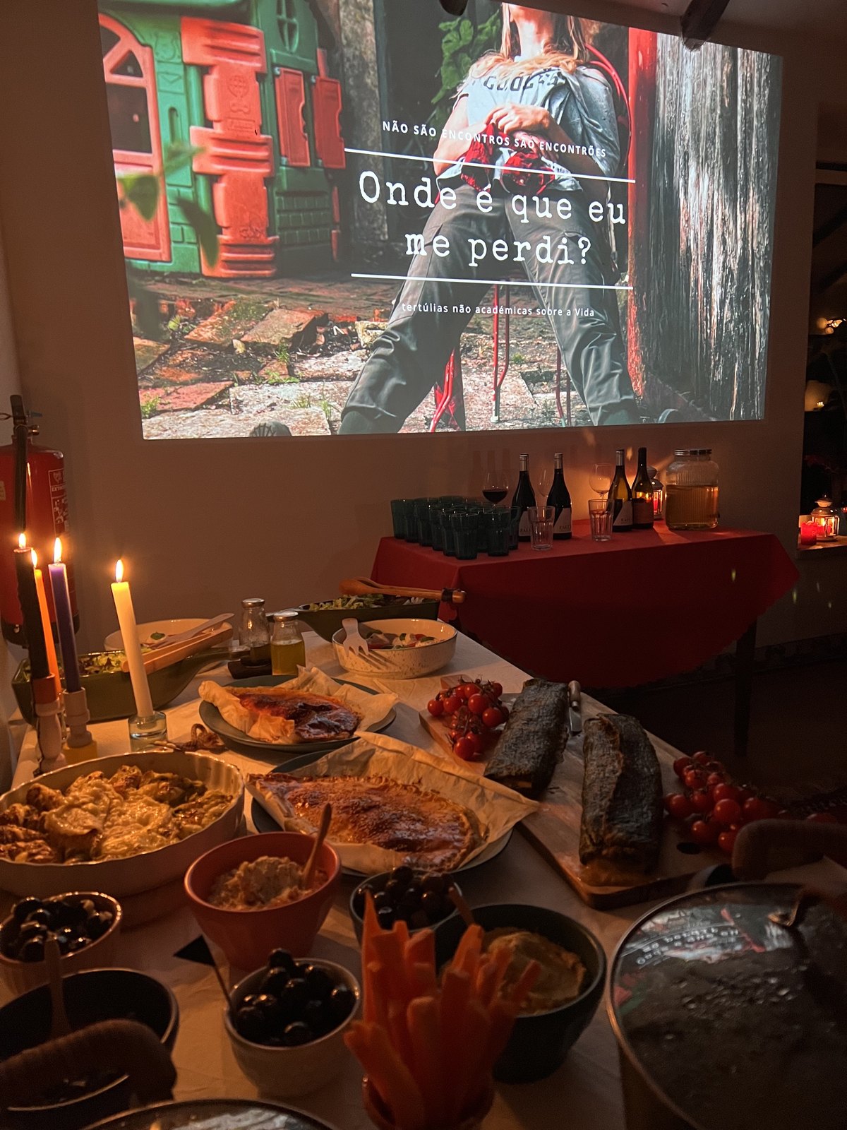 O cartaz de Onde é que eu me perdi? projetado numa parede, com a mesa de jantar posta em baixo