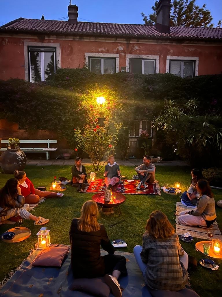 Grupo reunido num jardim ao anoitecer, &agrave; volta de lanternas e uma fogueira
