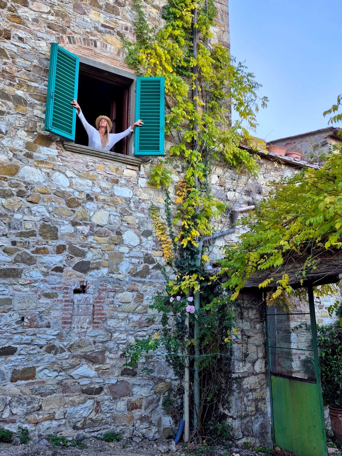 Isabel Saldanha de braços abertos numa janela antiga, rodeada de verde